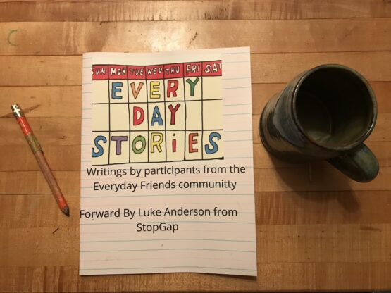 A photo of the Every Day Stories book on a wooden table. The title of the book is written in a colourful font. There is a pencil and ceramic mug nearby.